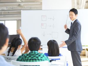 ホワイトボードで割り算を教える男性と学習する小学生